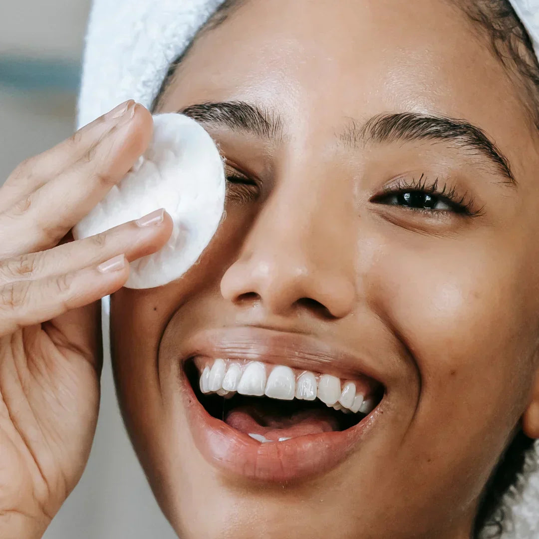 Woman smiling while applying Mòkah Soothè Hydrating Toner with a cotton pad.